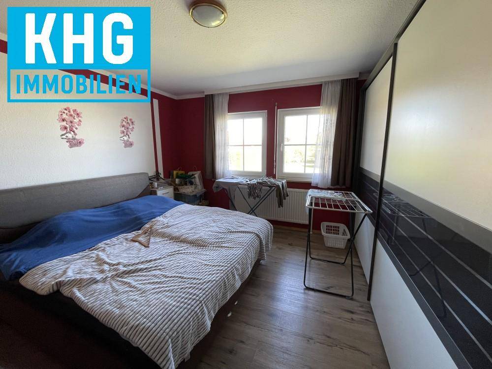 Schlafzimmer mit Doppelbett, Kleiderschrank und zwei Fenstern, die viel Licht hereinlassen.