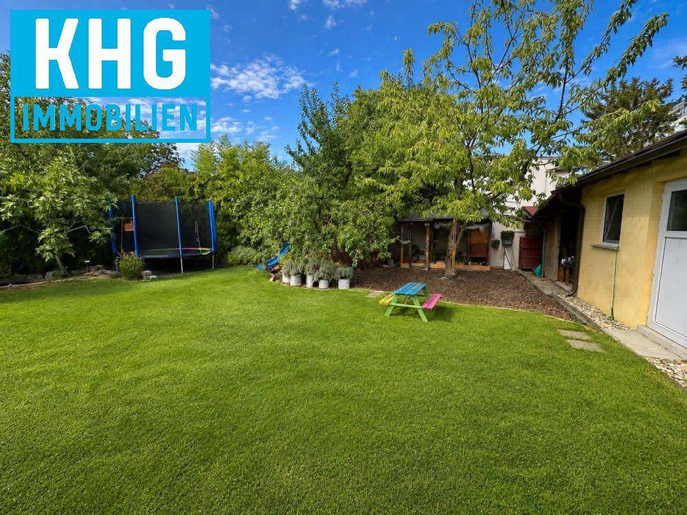 Großer grüner Garten mit Rasenfläche, Bäumen, Trampolin und einem kleinen Picknicktisch.