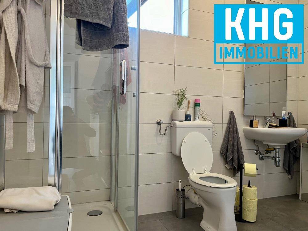 Modern gefliestes Badezimmer mit Duschkabine, Toilette und Waschbecken.