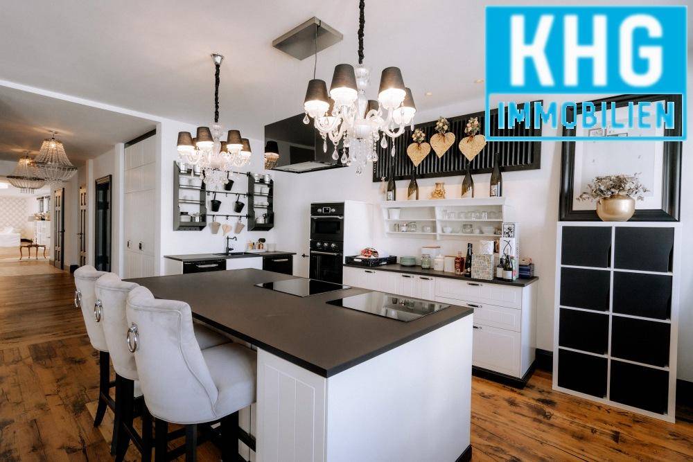 Moderne Küche mit großer Kücheninsel, schwarzen Arbeitsplatten und eleganten Kronleuchtern.