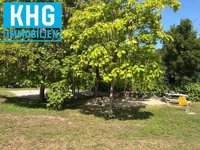 Schattiger Gartenbereich mit großen Bäumen und einem kleinen Spielplatz für Kinder.
