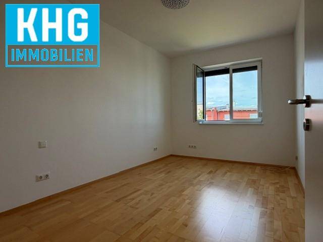 Helles, leeres Zimmer mit Holzboden und einem Fenster, das viel Tageslicht hereinlässt.