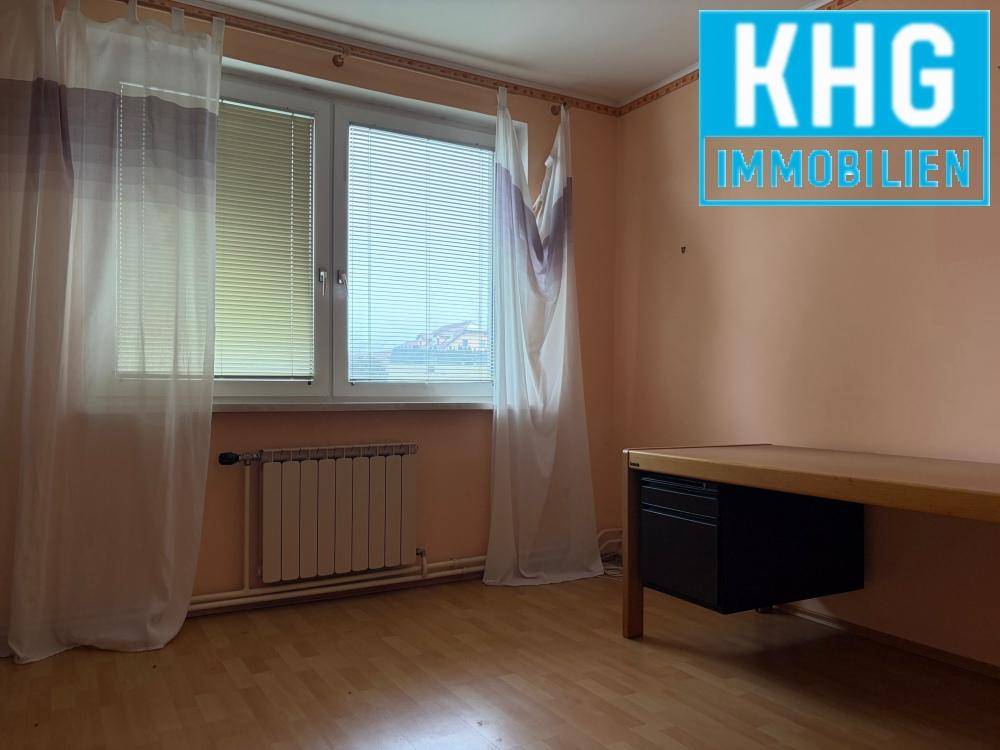 Helles Zimmer mit Laminatboden, großem Fenster und Heizkörper unter dem Fenster.
