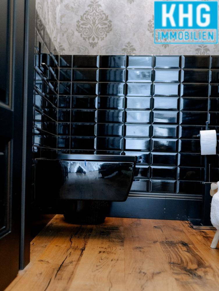 Modernes WC mit glänzenden schwarzen Fliesen und einer wandhängenden Toilette.