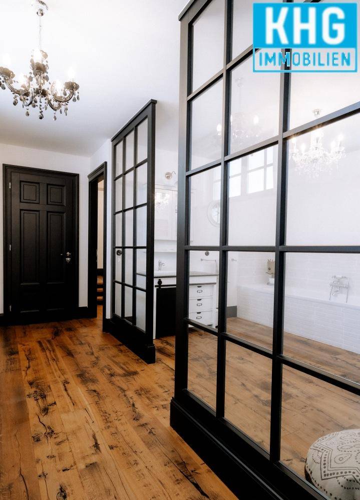 Eleganter Flur mit Holzboden, schwarzen Türen und einer stilvollen Glasabtrennung.