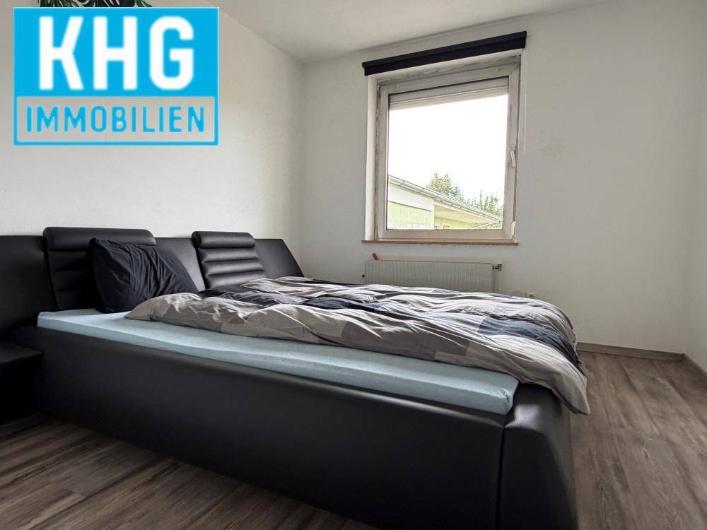 Schlafzimmer mit schwarzem Bett, Laminatboden und Fenster mit Heizkörper.