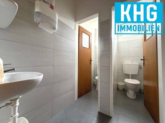 Moderner Toilettenbereich mit grauen Fliesen, Waschbecken und separaten Kabinen.