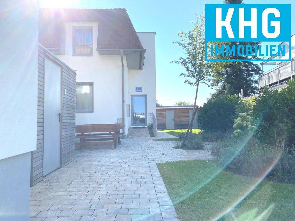 Außenansicht eines modernen Hauses mit gepflastertem Hof, Gartenbereich und einer Holzbank.