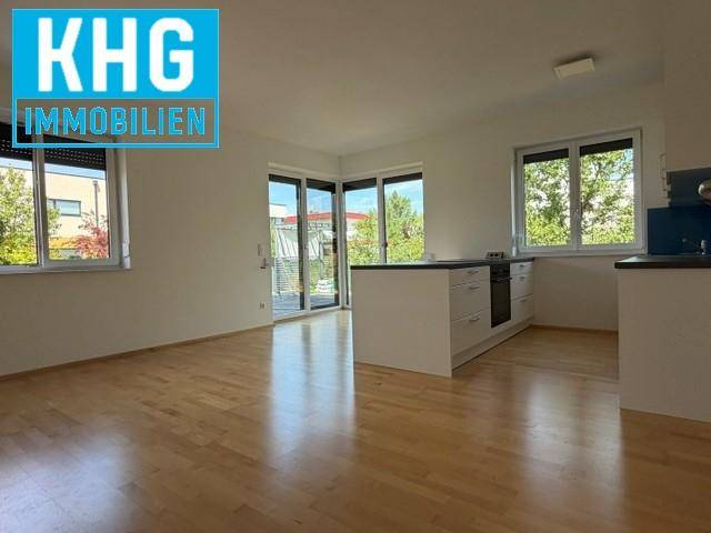 Heller offener Wohnbereich mit Holzboden, großen Fenstern und Zugang zu einem Außenbereich.