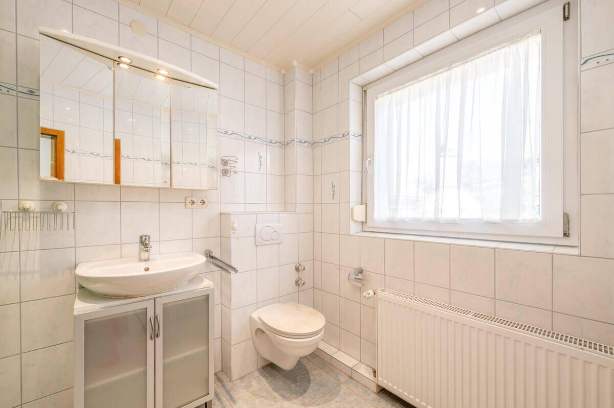 Kleines Badezimmer mit WC, Waschbecken und Fenster, hell gefliest.
