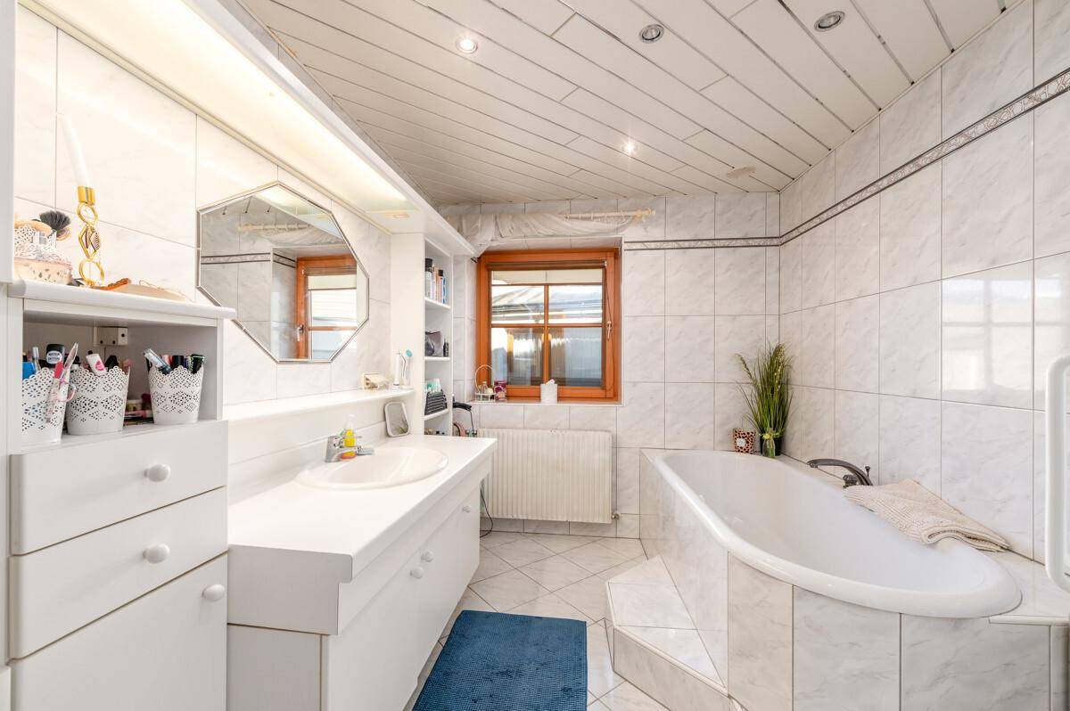 Geräumiges Badezimmer mit Badewanne, Einzelwaschbecken und weiß getäfelter Holzdecke.