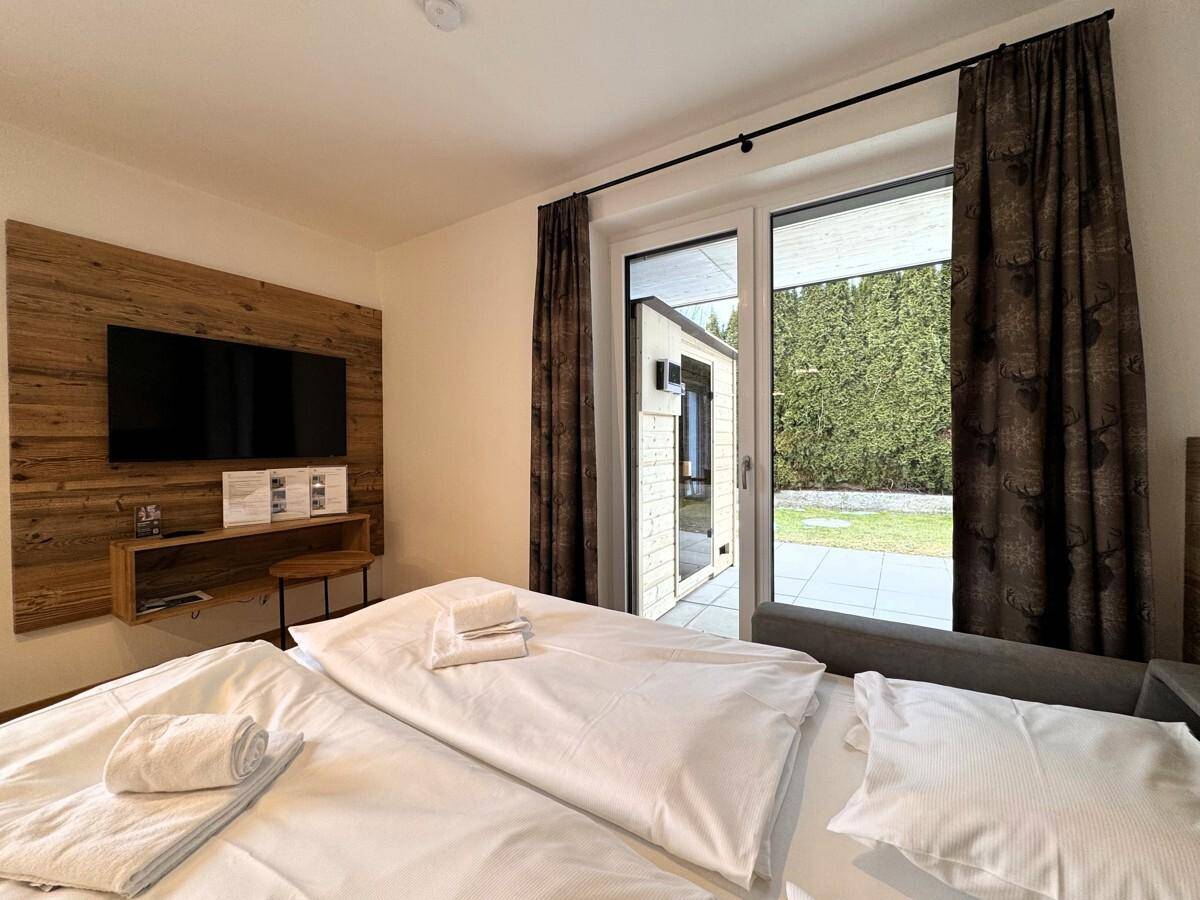 Schlafzimmer mit Doppelbett, Holzwand und direktem Zugang zur Terrasse oder zum Garten.
