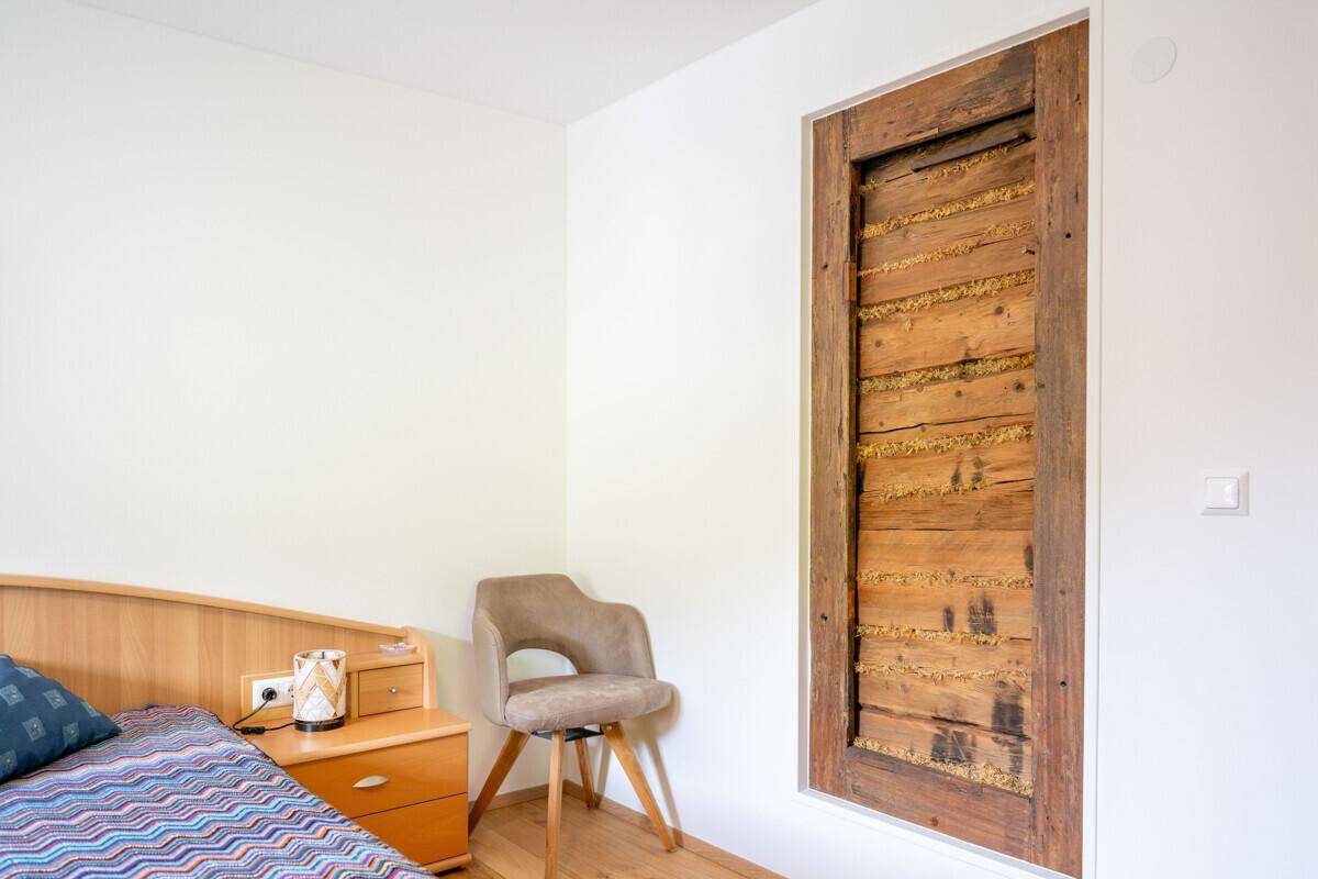 Detailansicht eines dekorativen Holzelements an der Wand in einem hellen Schlafzimmer.