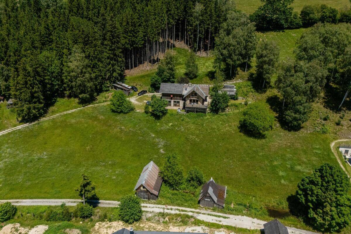 Luftaufnahme eines Anwesens mit Haupthaus, Nebengebäuden, weiten Wiesen und Wäldern.