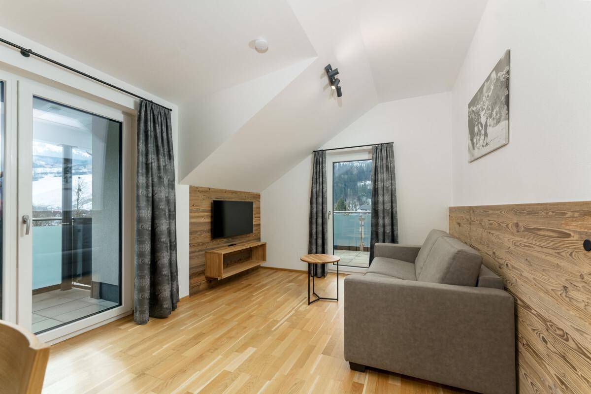Gemütliches Wohnzimmer mit Schlafsofa, Holzakzenten und Balkonzugang mit Bergblick.
