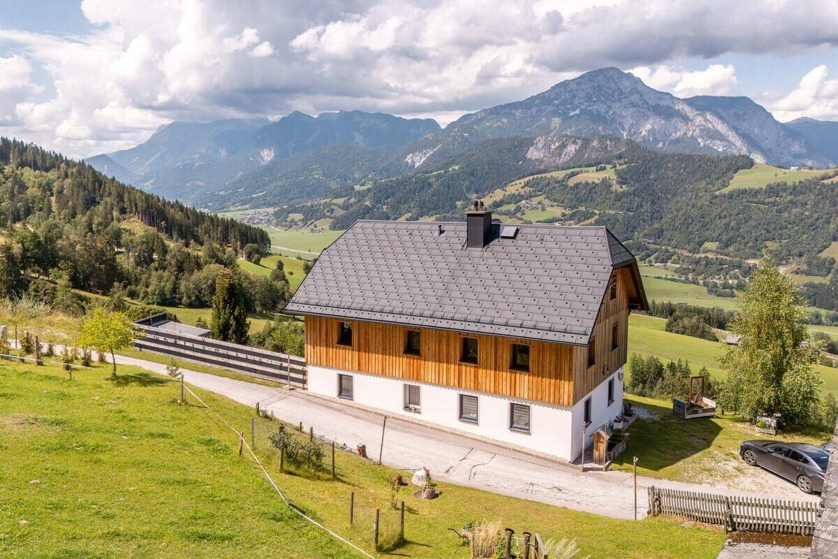 Charmantes Holzhaus mit dunklem Dach, umgeben von grünen Hügeln und majestätischen Bergen.