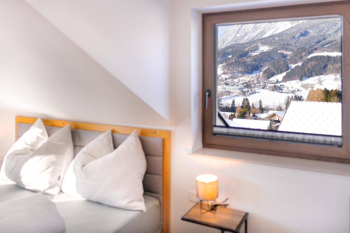 Gemütliches Schlafzimmer mit Holzboden, Dachschräge und Fensterblick auf ein verschneites Dorf.