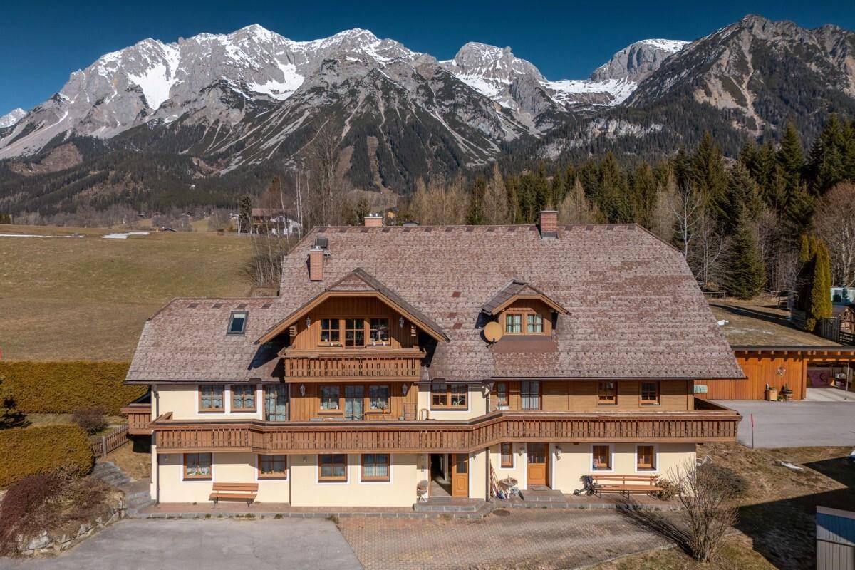 Frontansicht eines traditionellen Gebäudes mit Holzbalkonen vor einer beeindruckenden Bergkulisse.