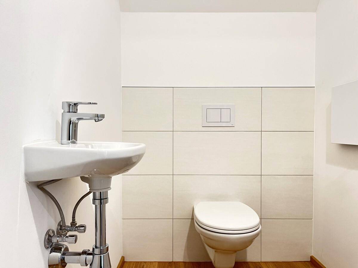 Kleines Gäste-WC mit wandhängender Toilette, kleinem Waschbecken und beigefarbenen Wandfliesen.