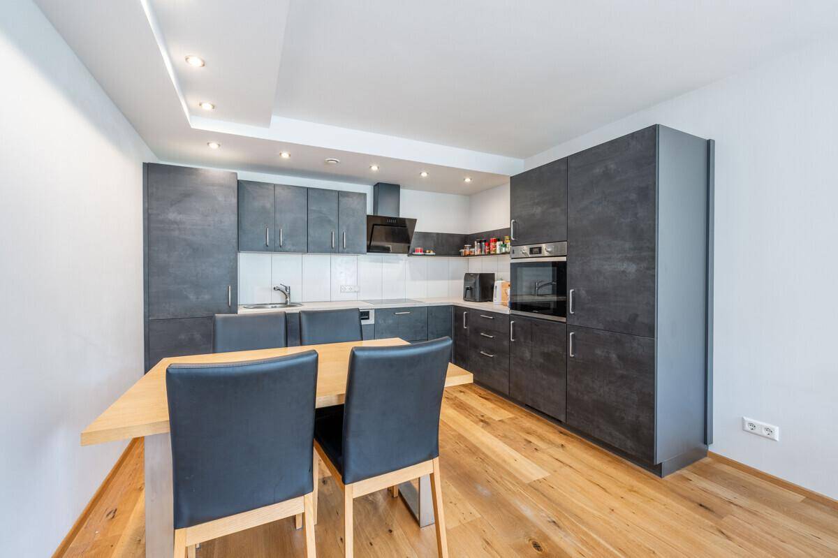 Moderne Küche mit dunklen Schränken, Holztisch und integrierten Geräten in hellem Ambiente.