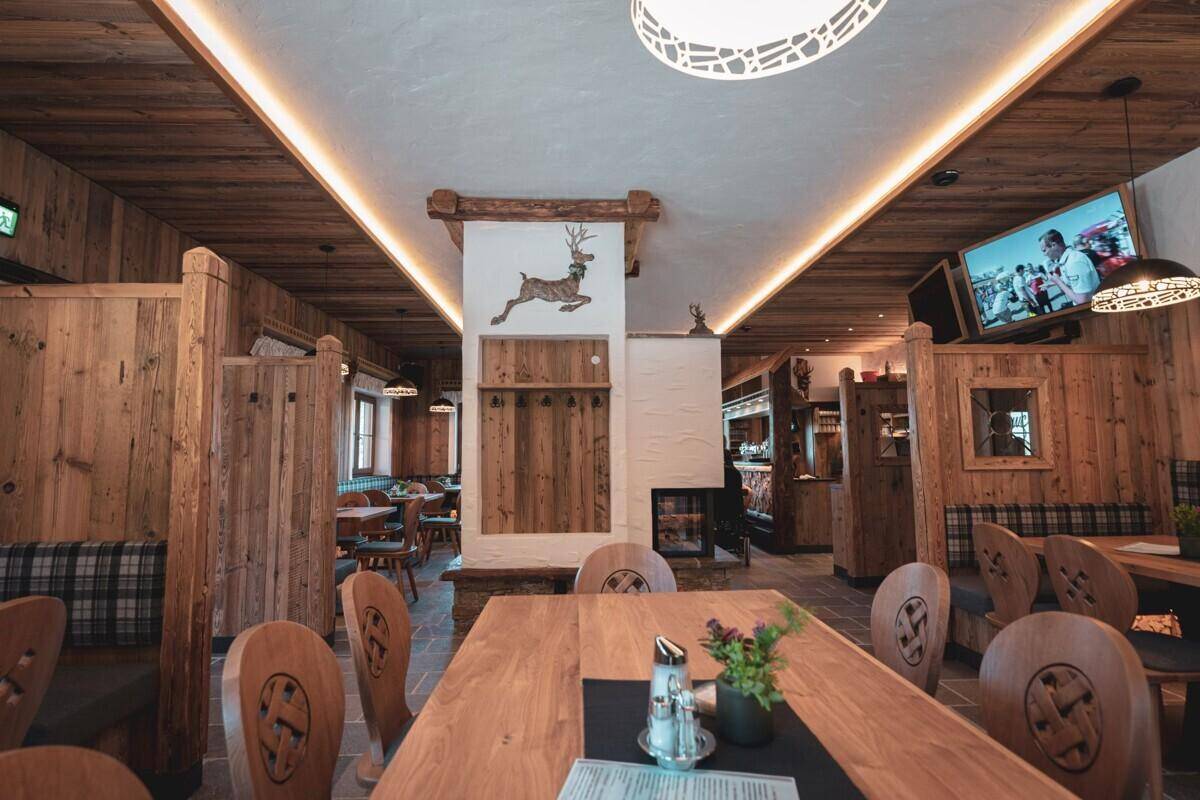 Gemütlicher Speisesaal im alpinen Stil mit Holztäfelung, Holztischen und Hirsch-Dekoration.