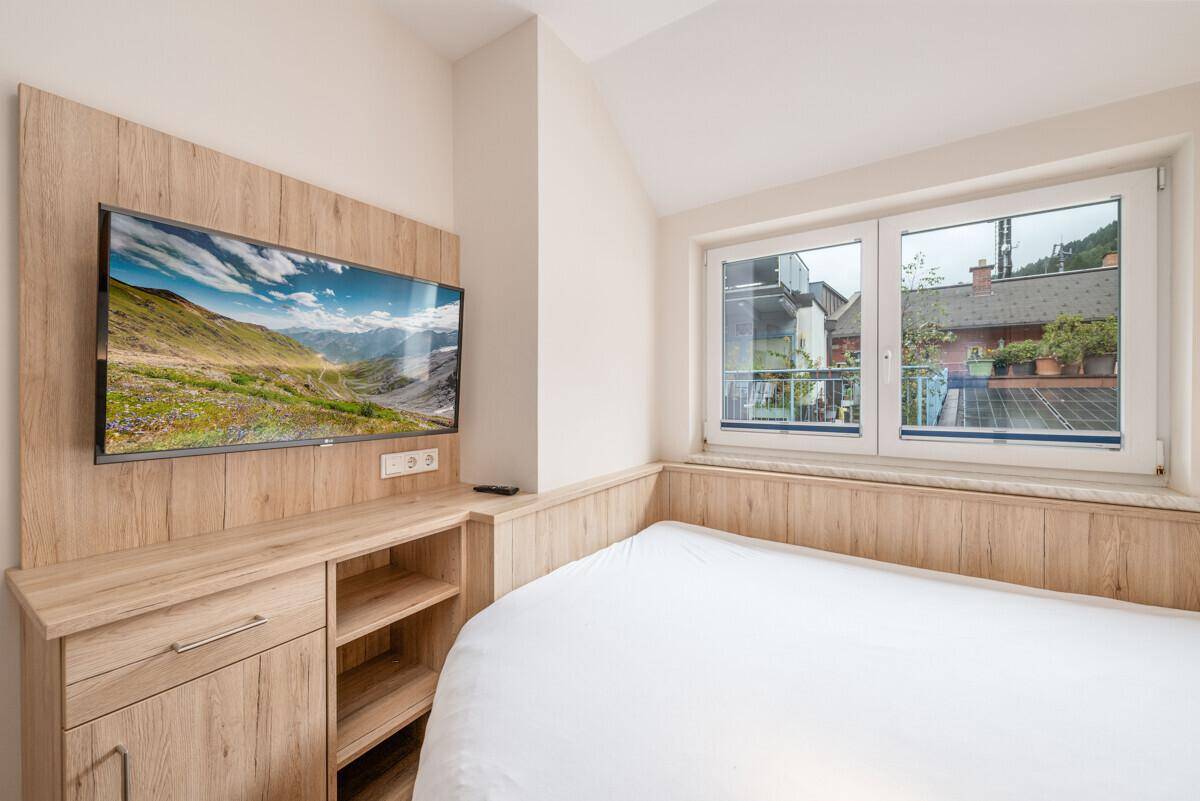 Gemütliches Einzelzimmer mit Bett, Wandpaneelen aus Holz und einem Flachbildfernseher.