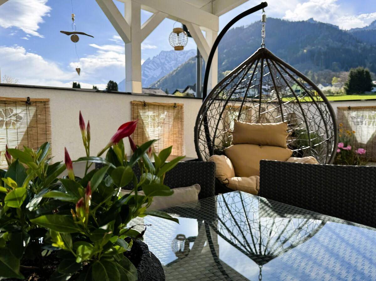 Detailansicht der Terrasse mit Hängesessel und Pflanzen, umgeben von einer idyllischen Bergkulisse.