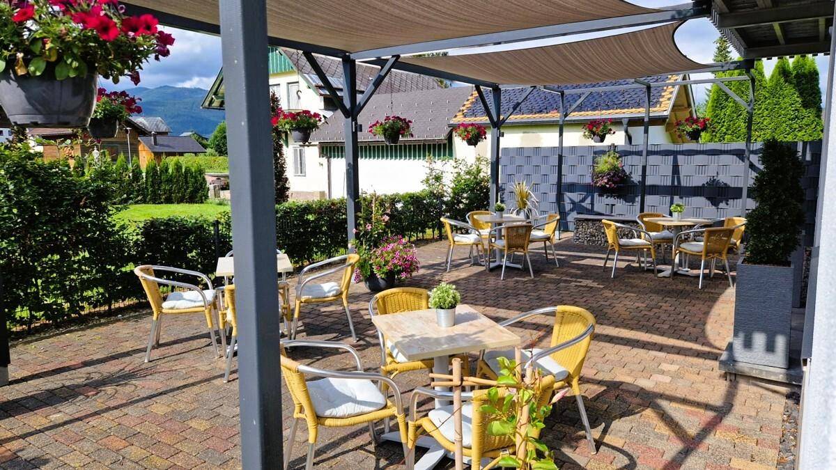 Einladender Terrassenbereich mit mehreren Sitzgruppen unter einer schattenspendenden Pergola.
