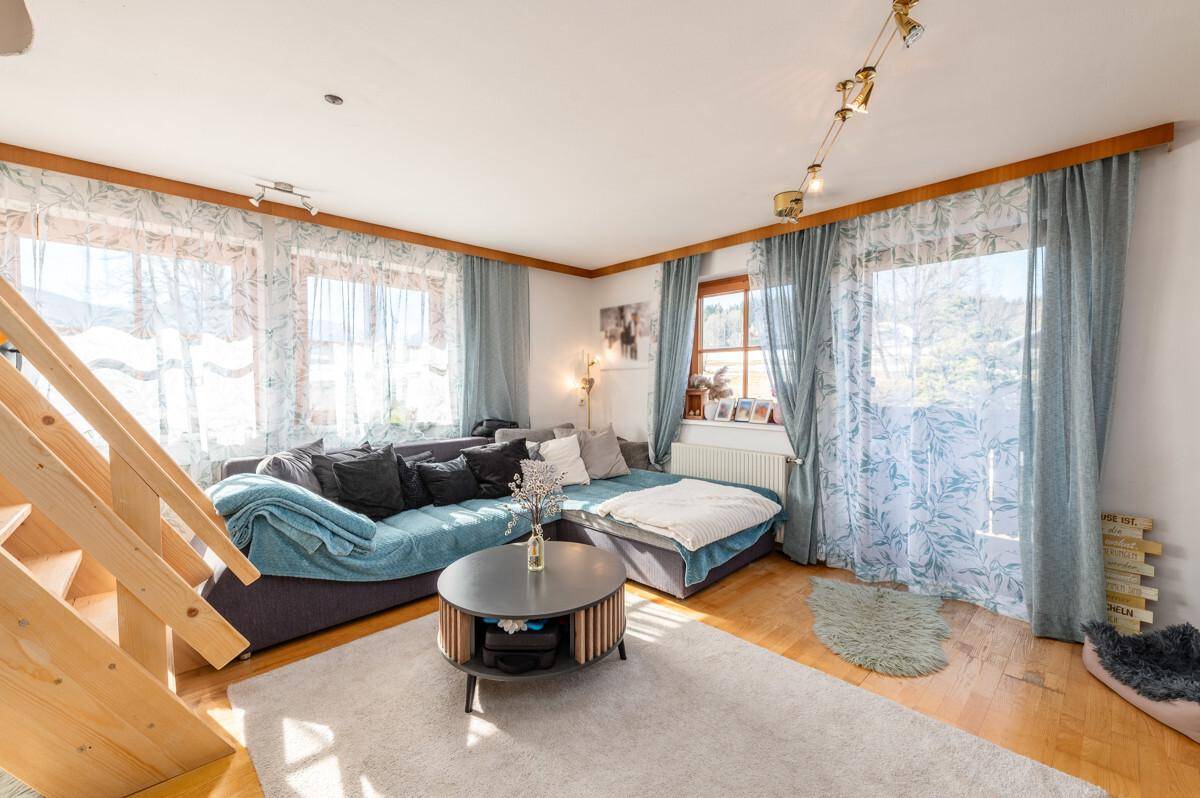 Geräumiges Wohnzimmer mit großem Sofa, Teppich und Zugang zu einem Balkon.