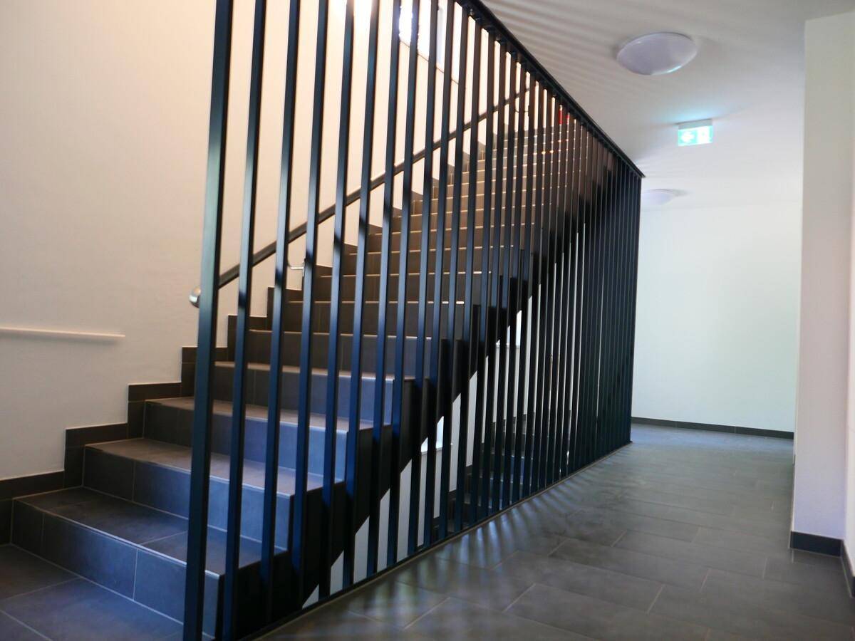 Modernes Treppenhaus mit dunklen Fliesen und minimalistischem Geländer.