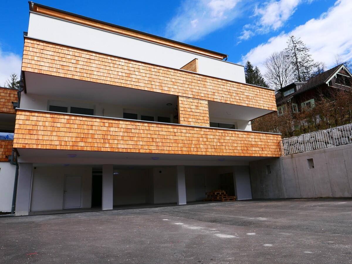 Neubau mit Holzschindelfassade und überdachten Parkplätzen im Erdgeschoss.