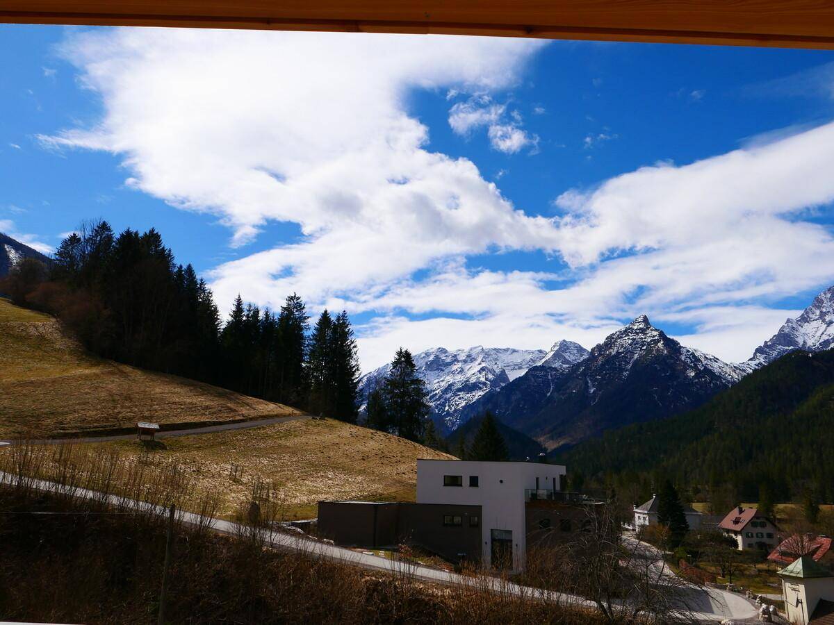 Weitläufiger Blick auf grüne Hügel und schneebedeckte Berggipfel unter blauem Himmel.