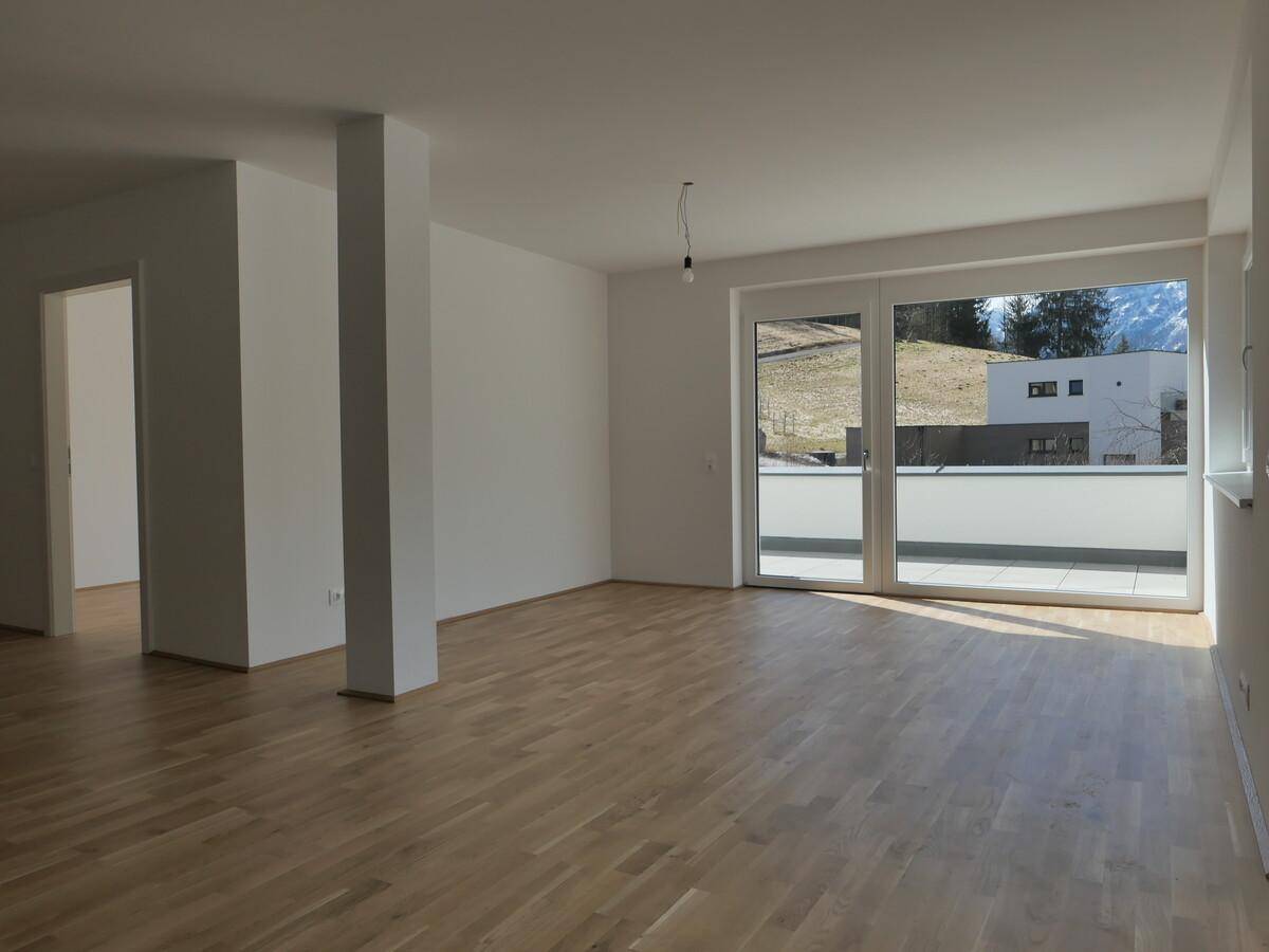 Geräumiger Wohnbereich mit hellem Holzboden und großen Fenstern zum Außenbereich.
