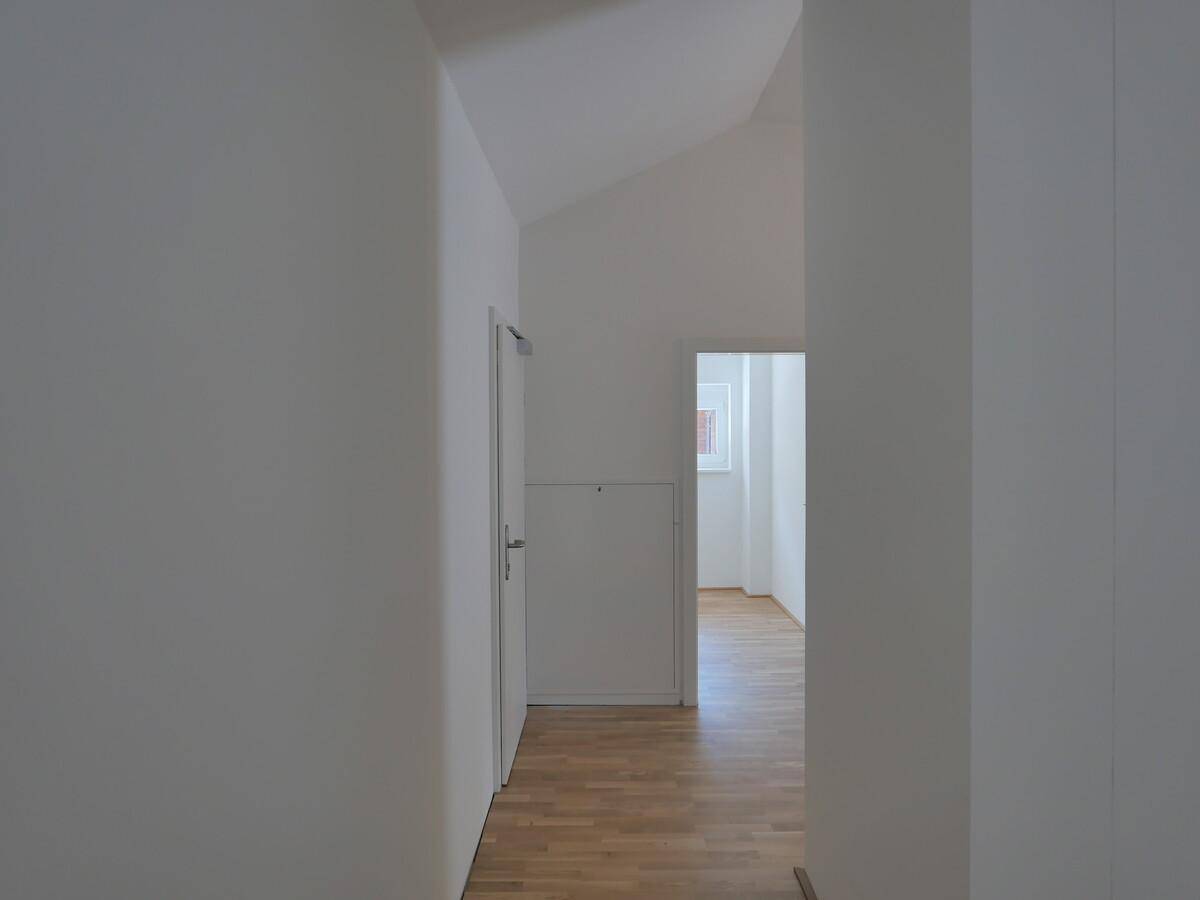 Heller Flur mit schrägen Decken und Holzboden, der zu weiteren Räumen führt.