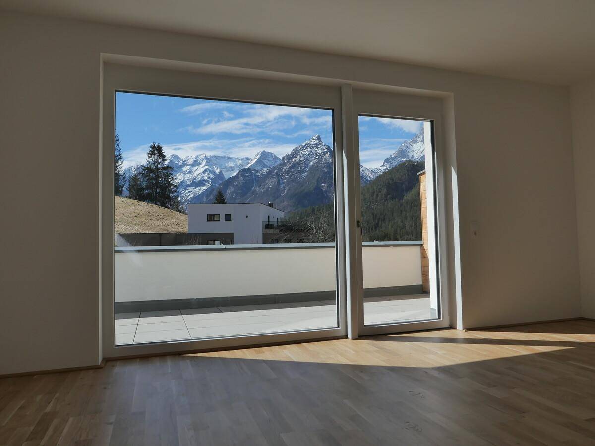 Lichtdurchfluteter Raum mit Holzboden und weitem Blick auf die umliegende Bergwelt.