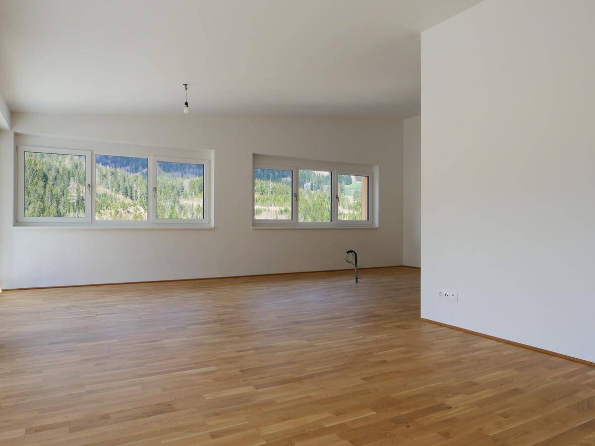 Heller Raum mit Holzboden und Fenstern, die einen Blick ins Grüne bieten.