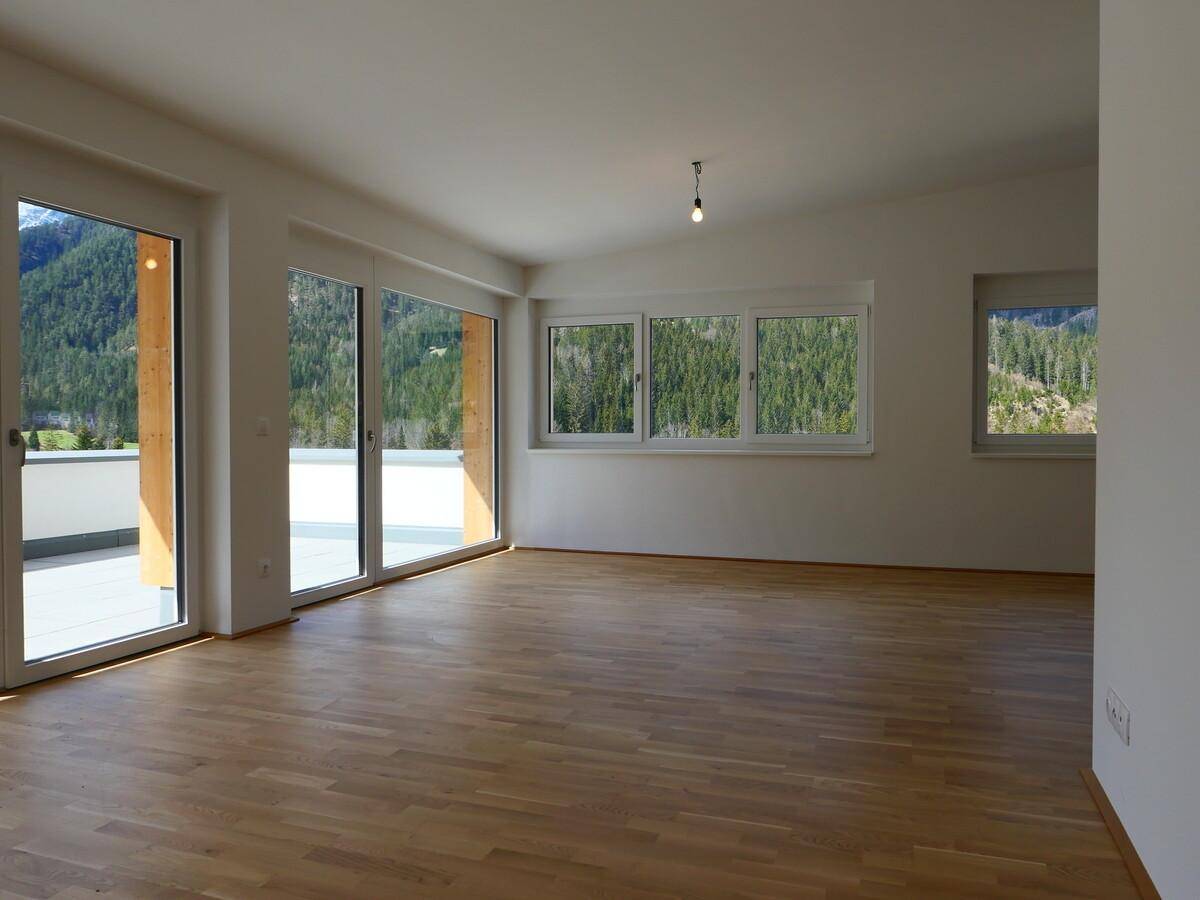 Lichtdurchfluteter Wohnbereich mit Holzboden und großen Fenstern mit Bergblick.