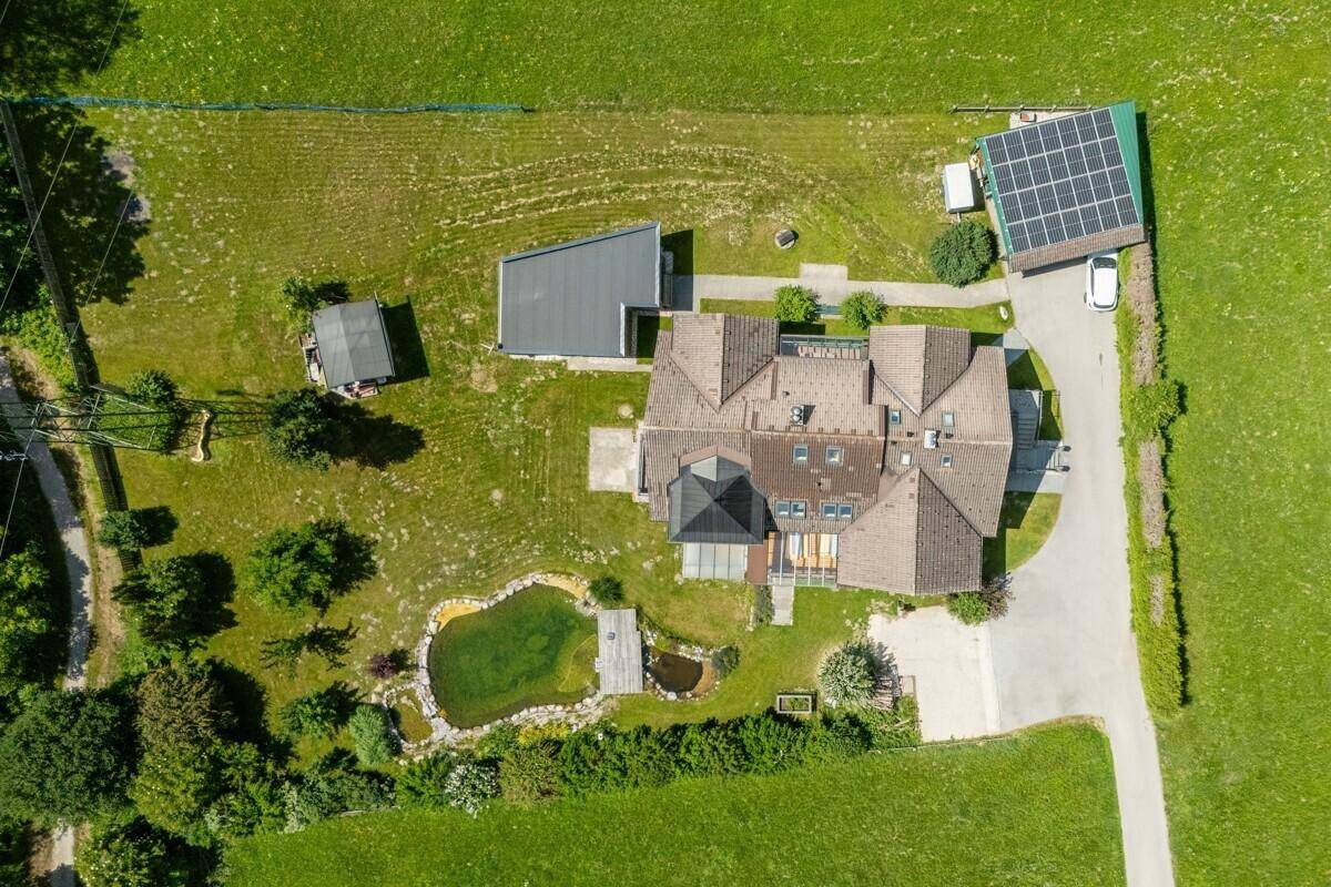 Draufsicht auf das Anwesen mit großem Garten, Naturteich und Photovoltaikanlage umgeben von Grünflächen.
