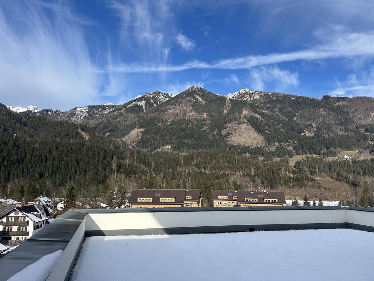 Blick von einer verschneiten Dachterrasse auf die umliegende Berglandschaft und ein Dorf im Tal.