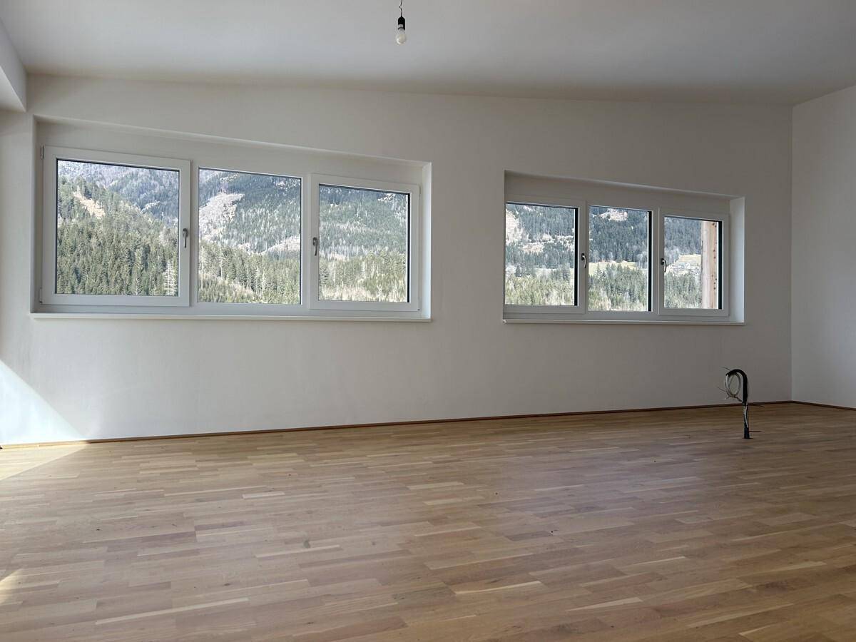 Helles Zimmer mit Holzboden und mehreren Fenstern, die einen schönen Blick auf die Berge ermöglichen.
