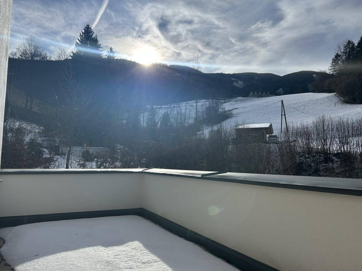 Sonniger Balkon mit teilweiser Schneedecke und Blick auf eine verschneite Hügellandschaft.