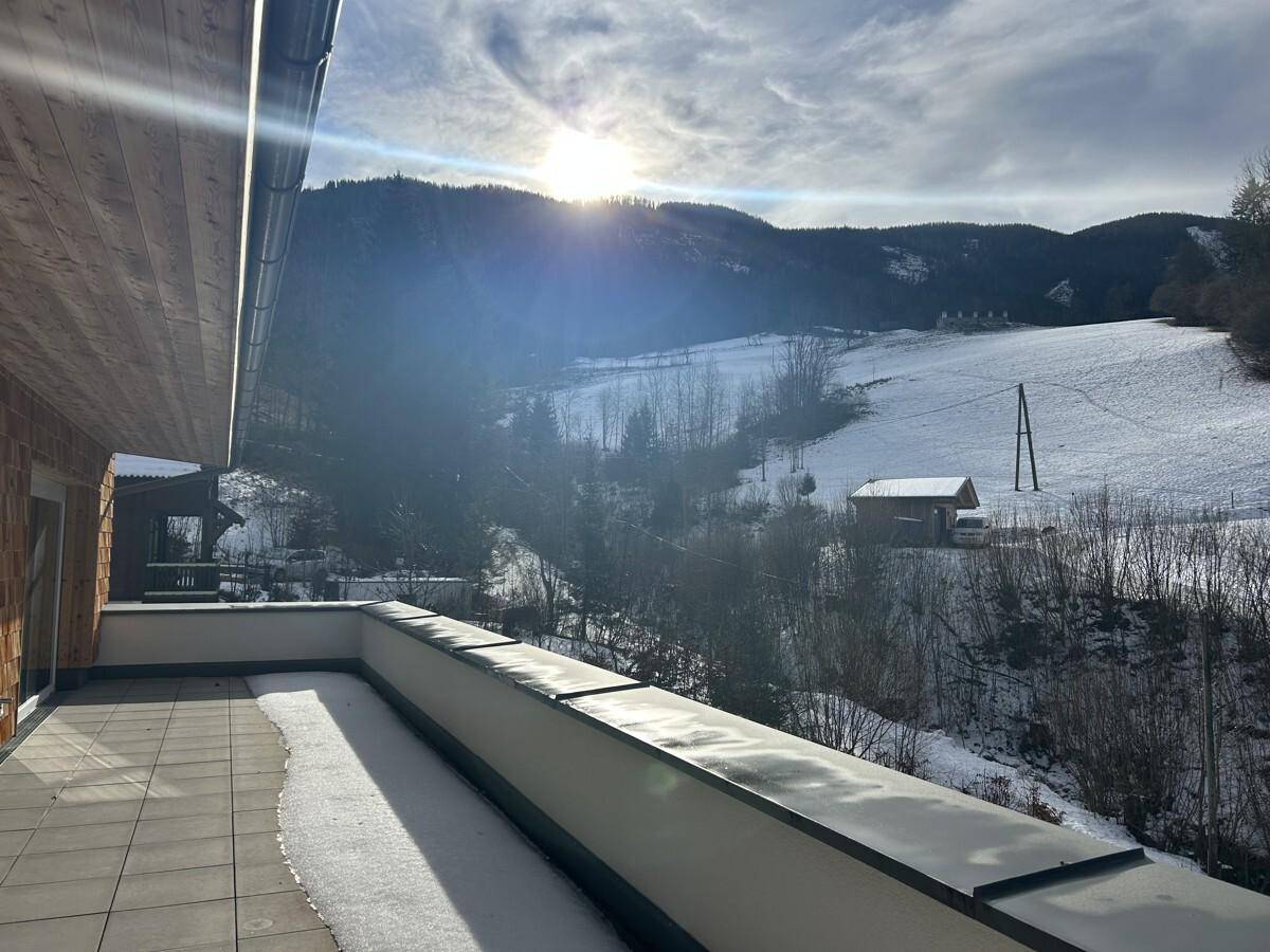 Sonniger Balkon mit teilweiser Schneedecke und Blick auf eine verschneite Hügellandschaft.