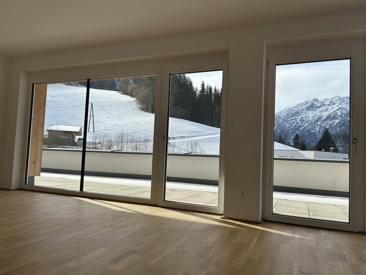 Geräumiges Wohnzimmer mit Holzboden und großen Fenstern, die einen weiten Bergblick bieten.