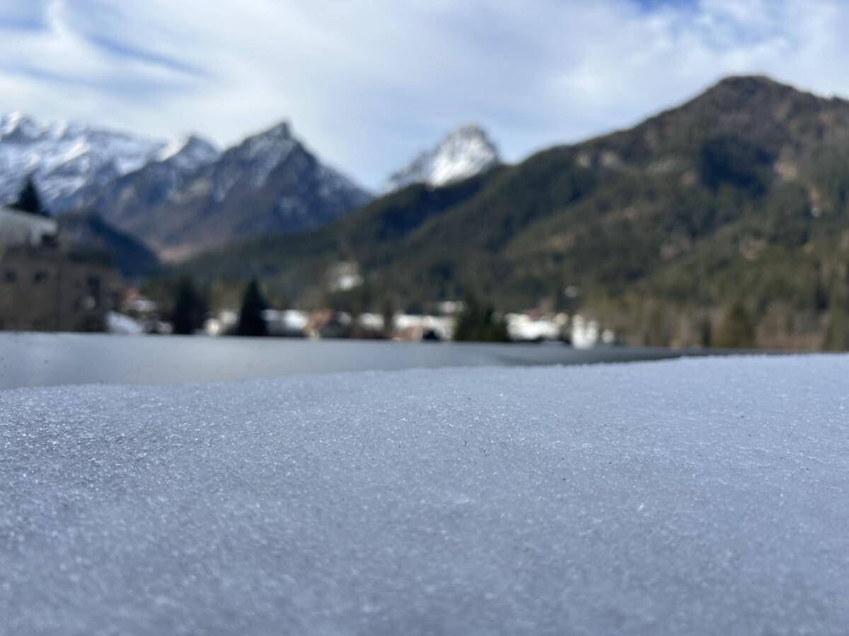 Nahaufnahme von Schnee auf einer Oberfläche mit unscharfem Blick auf die schneebedeckten Berge im Hintergrund.