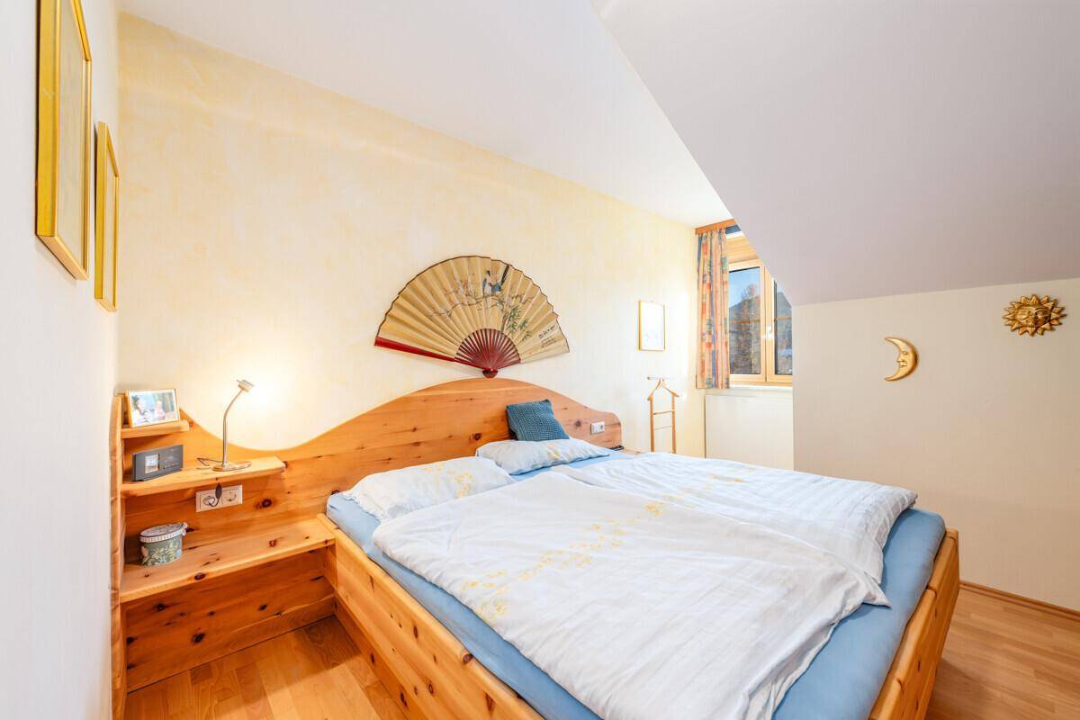 Schlafzimmer mit Holzbett, Dachschrägen und Fenster, hell und traditionell eingerichtet.
