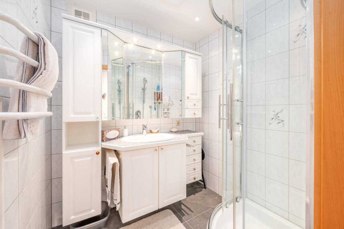 Helles Badezimmer mit Dusche, Waschbecken und Spiegelschrank, weiß gefliest.