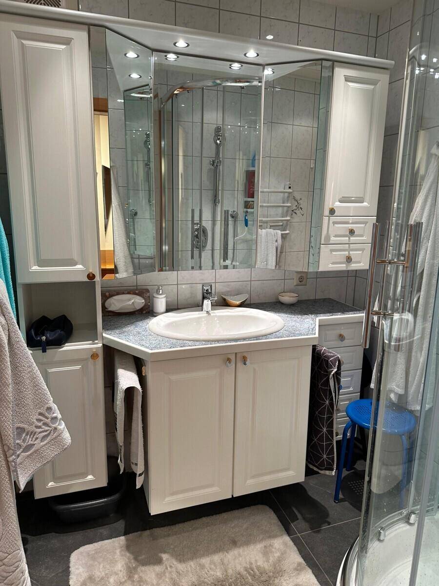 Badezimmer mit Waschbecken, Spiegelschrank und Dusche, weiß gefliest.