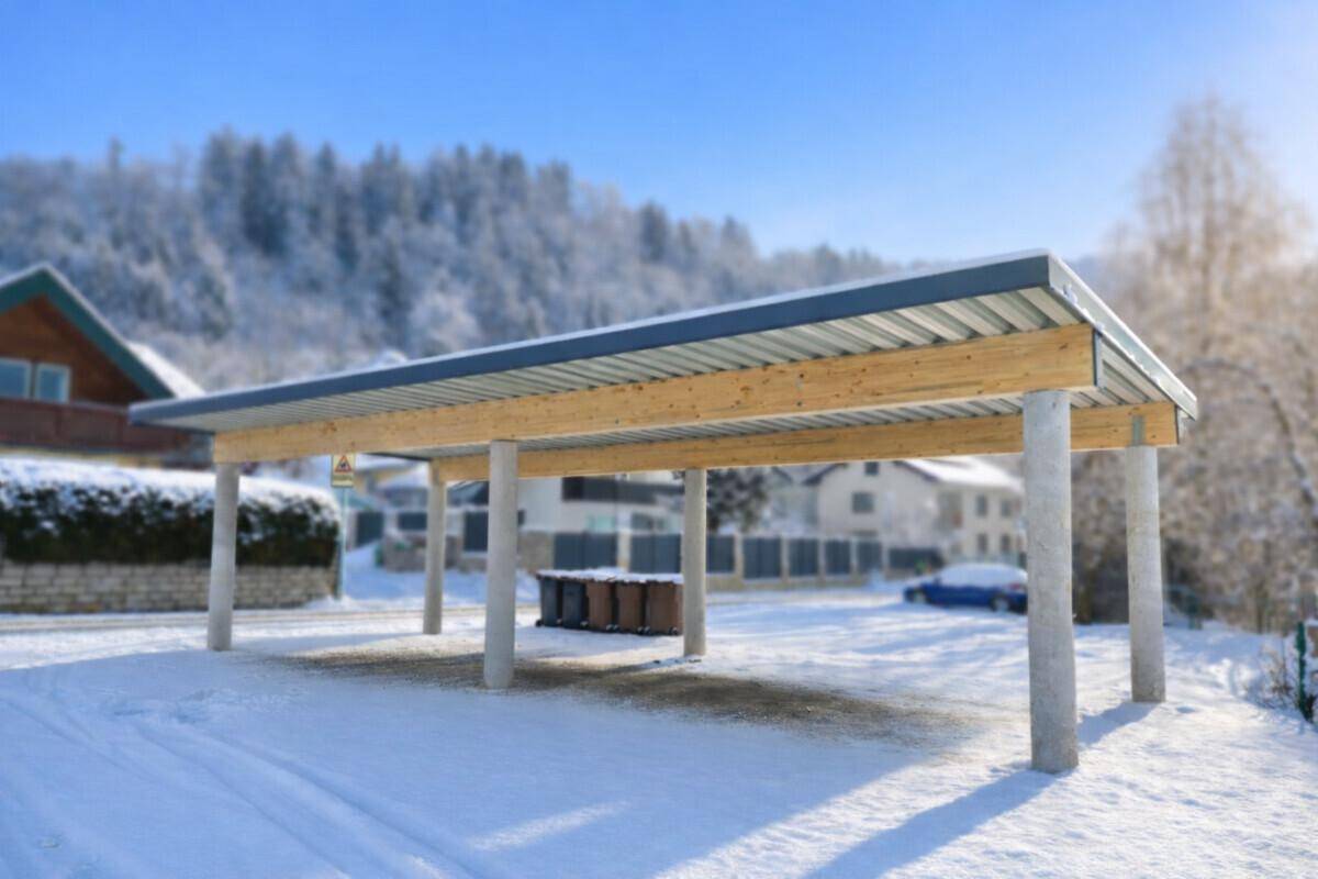 Freistehender Carport mit Holzdach und Betonsäulen in einer verschneiten ländlichen Umgebung.