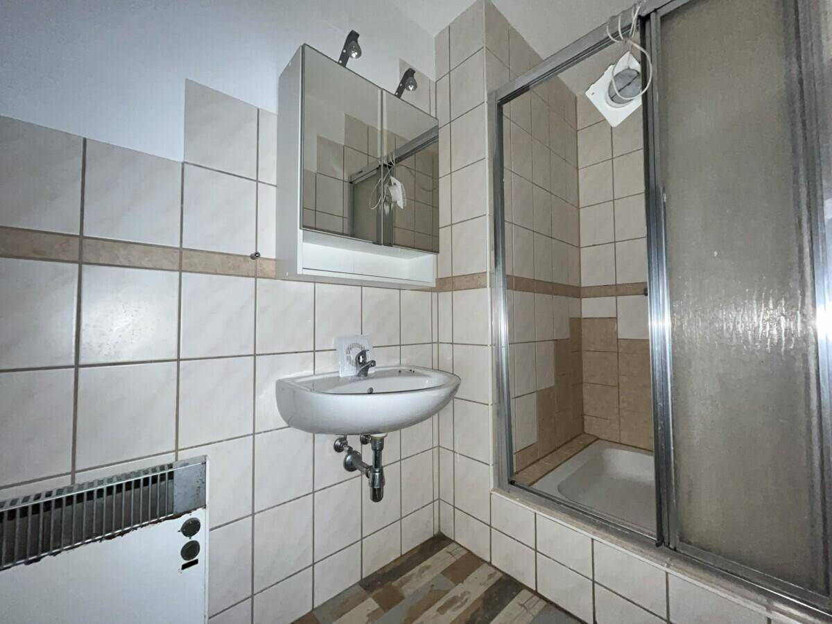 Funktionales Badezimmer mit Duschkabine, Einzelwaschbecken, Spiegelschrank und beigefarbenen Fliesen.