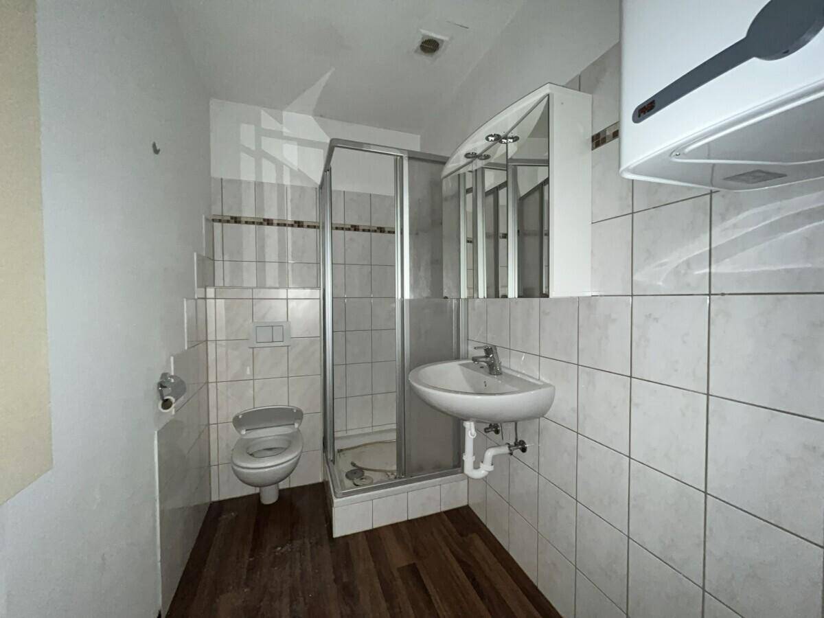 Badezimmer mit Duschkabine, wandhängendem WC, Waschbecken und weiß gefliesten Wänden.